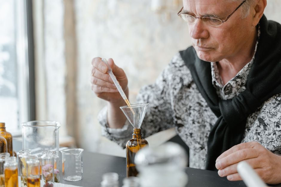Senior adult blending essential oils using a dropper and brown glass bottles in a cozy indoor setting.